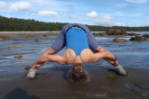 Jenny doing a variation of Wide Legged Forward Fold (Prasarita Padottanasana), this time holding onto her ankles and keeping her elbows out to the side, at Sand Point Beach, Olympic National Park, Washington State (Photo by Ian Hatter).